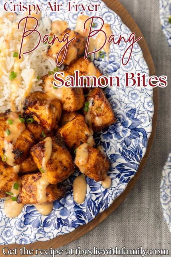 crispy air fryer bang bang salmon bites drizzled with sauce served with ice on a blue and white floral plate with text overlay describing the photo