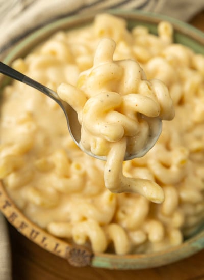 A spoonful of super creamy macaroni and cheese is being held over a bowl.