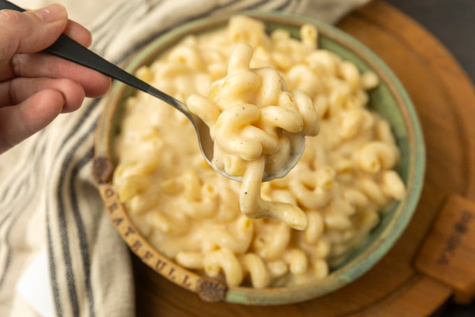 A spoonful of super creamy macaroni and cheese is being held over a bowl.