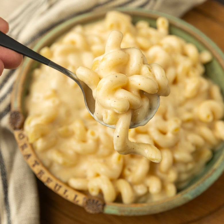 A spoonful of super creamy macaroni and cheese is being held over a bowl.
