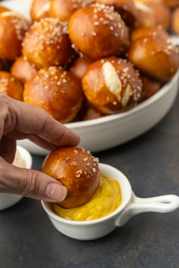 A hand dipping a sourdough discard pretzel bite into mustard.