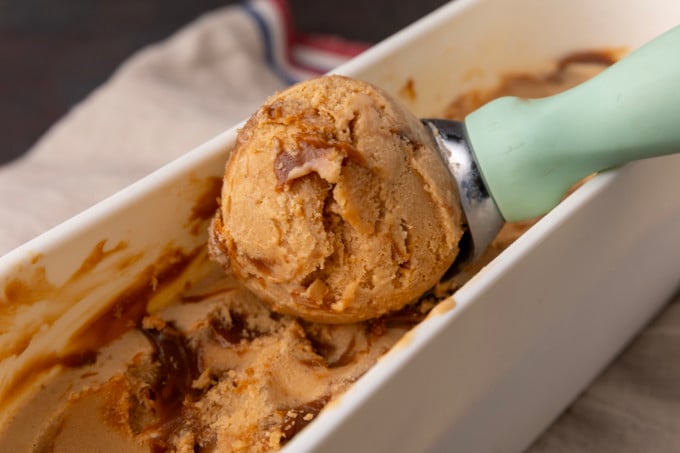 A scoop of dulce de leche ice cream is being scooped into a bowl.
