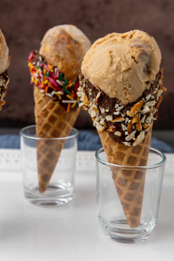 Three dulce de leche ice cream cones with toppings on them.
