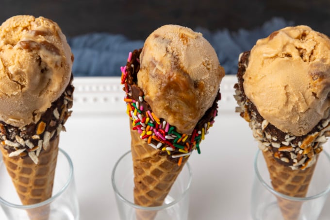 Three dulce de leche ice cream cones with toppings on top.