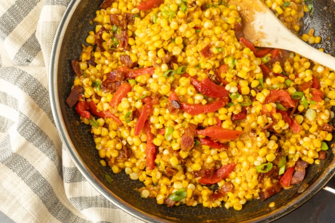 fried sweet corn with bacon, green onions and roasted red peppers in a bowl