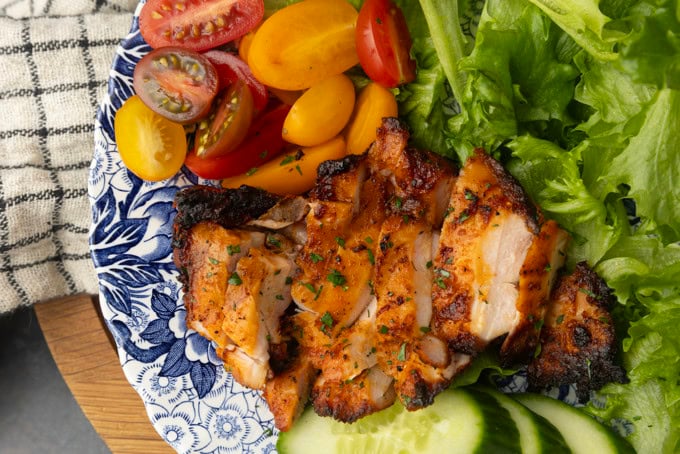 chicken thighs grilled on a pellet grill on a plate with lettuce, tomatoes, and cucumbers