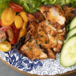 chicken thighs grilled on a pellet grill on a plate with lettuce, tomatoes, and cucumbers