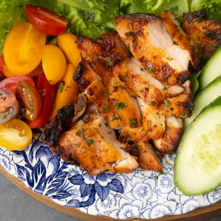 chicken thighs grilled on a pellet grill on a plate with lettuce, tomatoes, and cucumbers