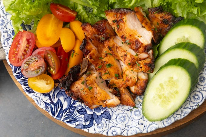 chicken thighs grilled on a pellet grill on a plate with lettuce, tomatoes, and cucumbers