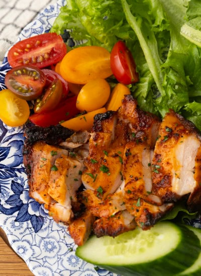 chicken thighs grilled on a pellet grill on a plate with lettuce, tomatoes, and cucumbers