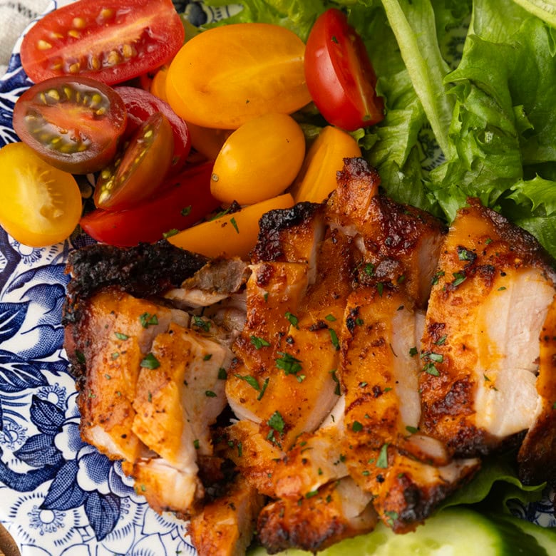 chicken thighs grilled on a pellet grill on a plate with lettuce, tomatoes, and cucumbers