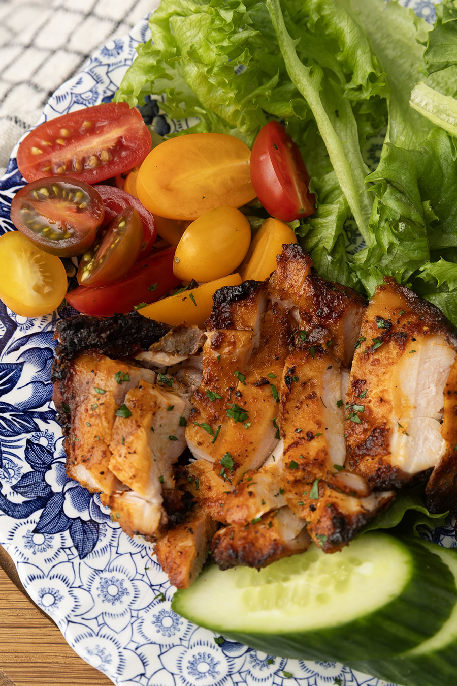 chicken thighs grilled on a pellet grill on a plate with lettuce, tomatoes, and cucumbers