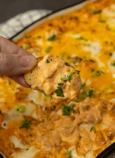 Buffalo chicken dip with a hand dipping a chip.