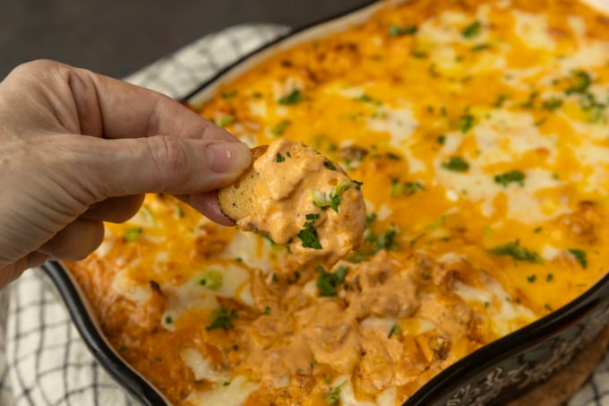 Buffalo chicken dip with a hand dipping a chip.