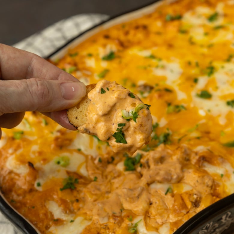 Buffalo chicken dip with a hand dipping a chip.