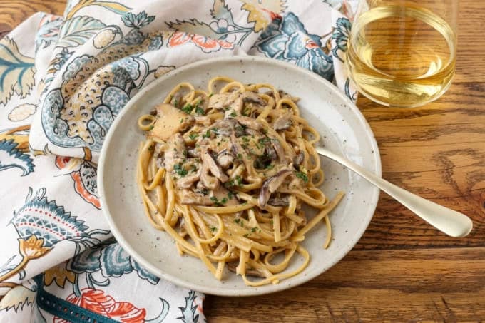 miso mushroom pasta with a fork on a plate with a glass of white wine