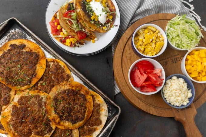 smash tacos on a pan and on stacked plates with toppings in bowls