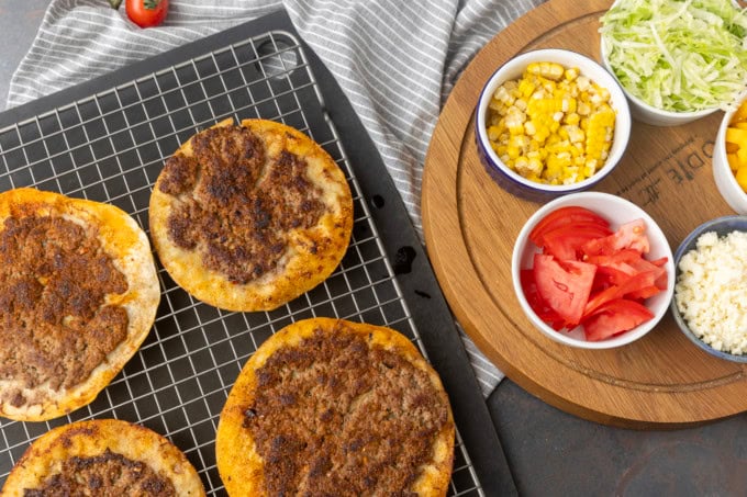 smash tacos on a cooling rack with toppings in bowls