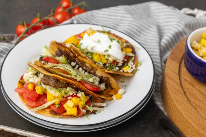 smash tacos on stacked plates with toppings in bowls