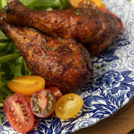 smoked chicken drumsticks on a blue and white plate with cherry tomatoes