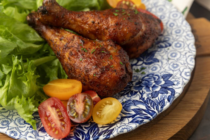 smoked chicken drumsticks on a blue and white plate with cherry tomatoes