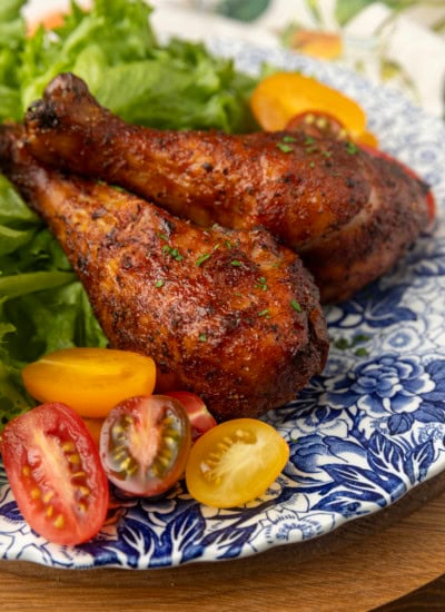 smoked chicken drumsticks on a blue and white plate with cherry tomatoes