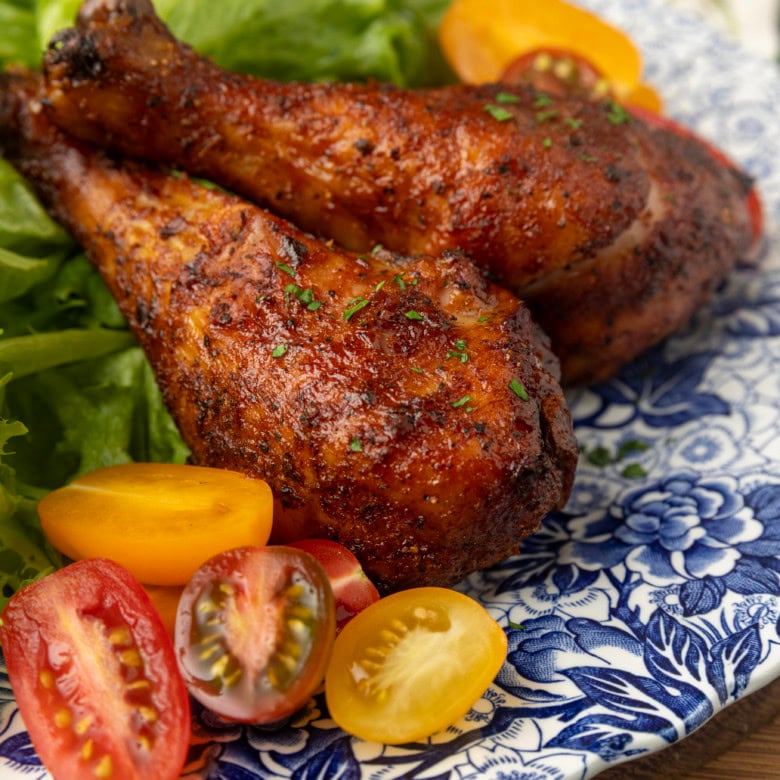 smoked chicken drumsticks on a blue and white plate with cherry tomatoes