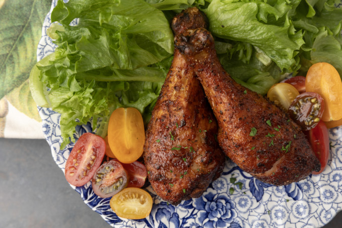 smoked chicken drumsticks on a blue and white plate with cherry tomatoes