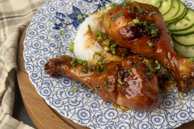 baked honey garlic chicken on rice with cucumbers on a blue and white plate