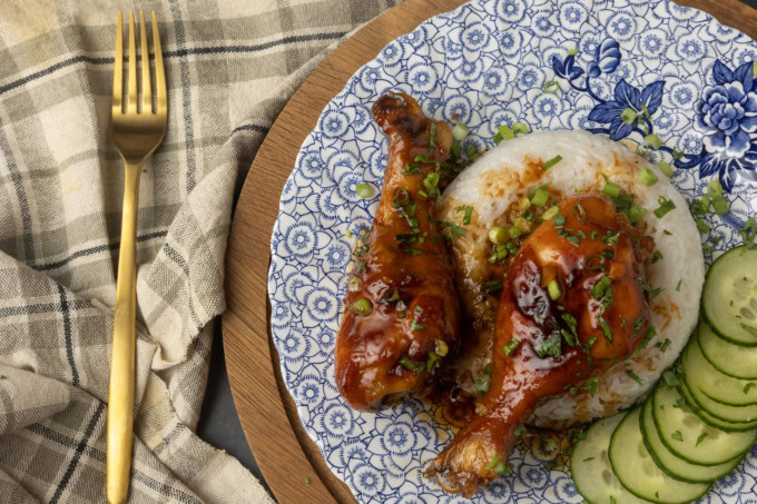 baked honey garlic chicken on rice with cucumbers on a blue and white plate