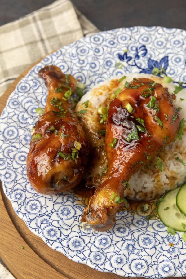 baked honey garlic chicken on rice with cucumbers on a blue and white plate