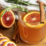 Orange tea in a mug with a slice of orange, a cinnamon stick, and a sprig of rosemary.