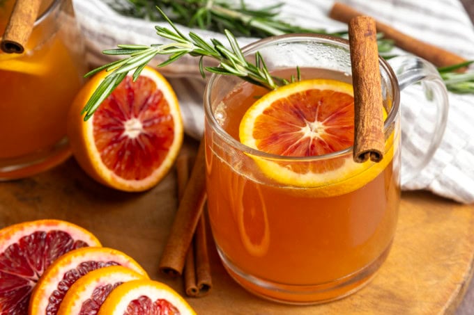 Orange tea in a mug with a slice of orange, a cinnamon stick, and a sprig of rosemary.