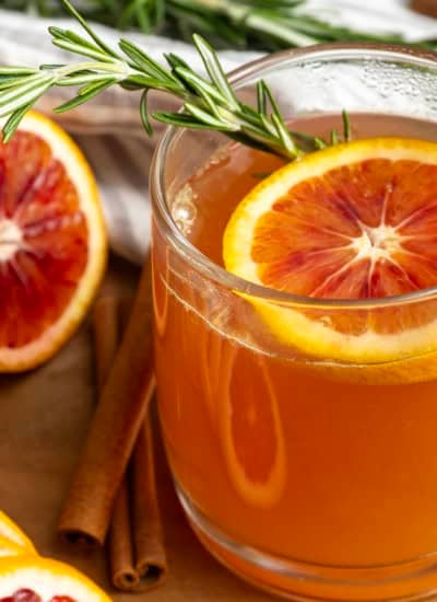 Orange tea in a mug with a slice of orange, a cinnamon stick, and a sprig of rosemary.