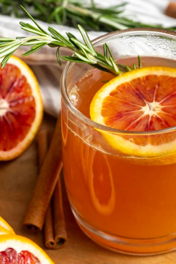 Orange tea in a mug with a slice of orange, a cinnamon stick, and a sprig of rosemary.