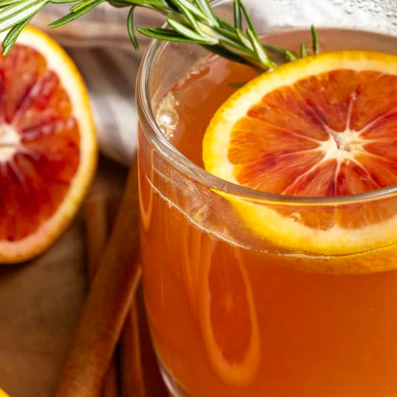 Orange tea in a mug with a slice of orange, a cinnamon stick, and a sprig of rosemary.