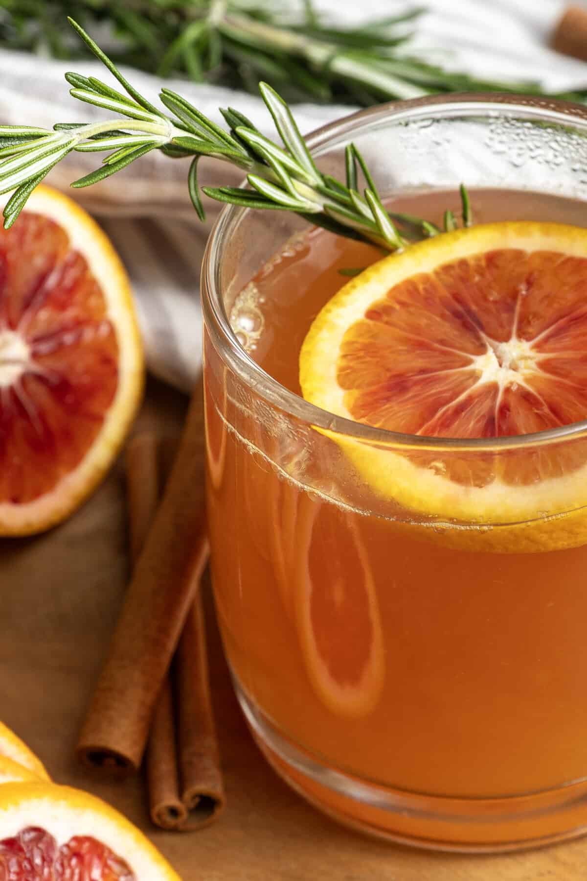 Orange tea in a mug with a slice of orange, a cinnamon stick, and a sprig of rosemary.