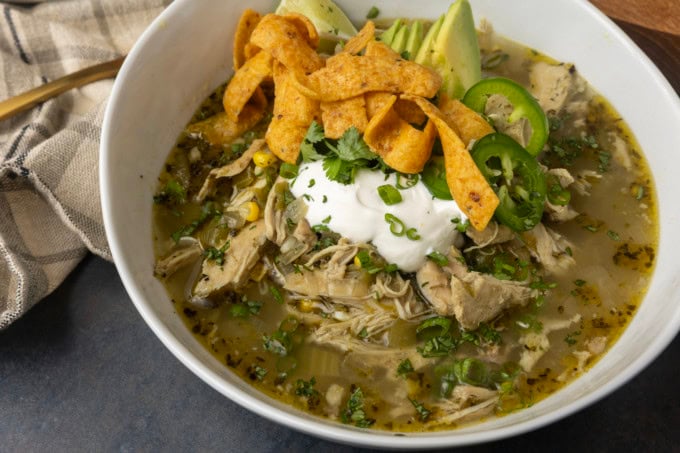 white bean chicken chili in a bowl with avocados, jalapenos, sour cream, cilantro, fritos, and lime wedges
