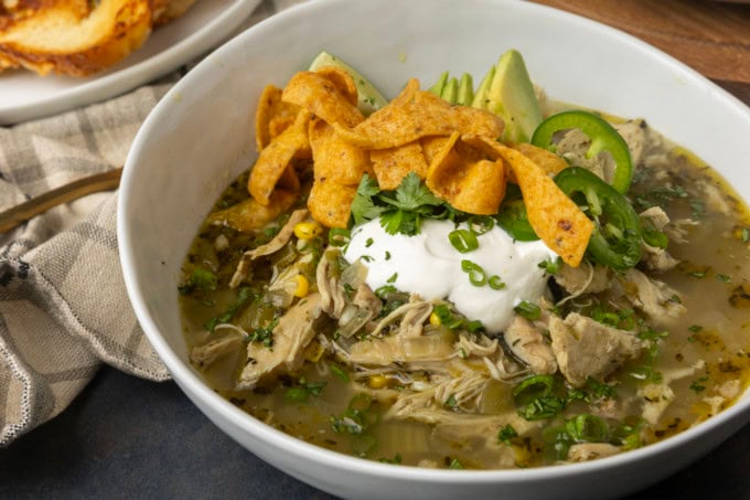 white bean chicken chili in a bowl with avocados, jalapenos, sour cream, cilantro, fritos, and lime wedges