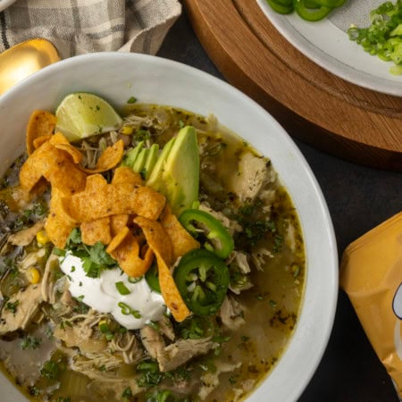 white bean chicken chili in a bowl with avocados, jalapenos, sour cream, cilantro, fritos, and lime wedges