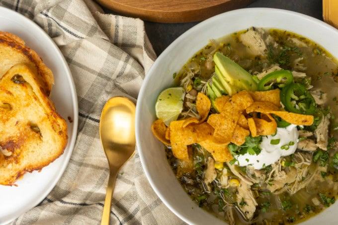 white bean chicken chili in a bowl with avocados, jalapenos, sour cream, cilantro, fritos, and lime wedges