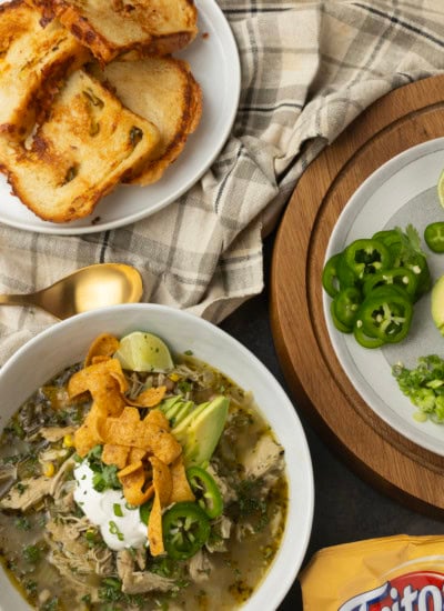 white bean chicken chili in a bowl with avocados, jalapenos, sour cream, cilantro, fritos, and lime wedges
