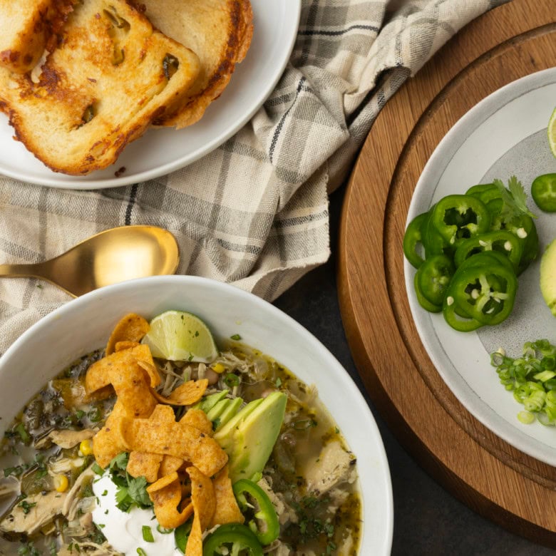 white bean chicken chili in a bowl with avocados, jalapenos, sour cream, cilantro, fritos, and lime wedges