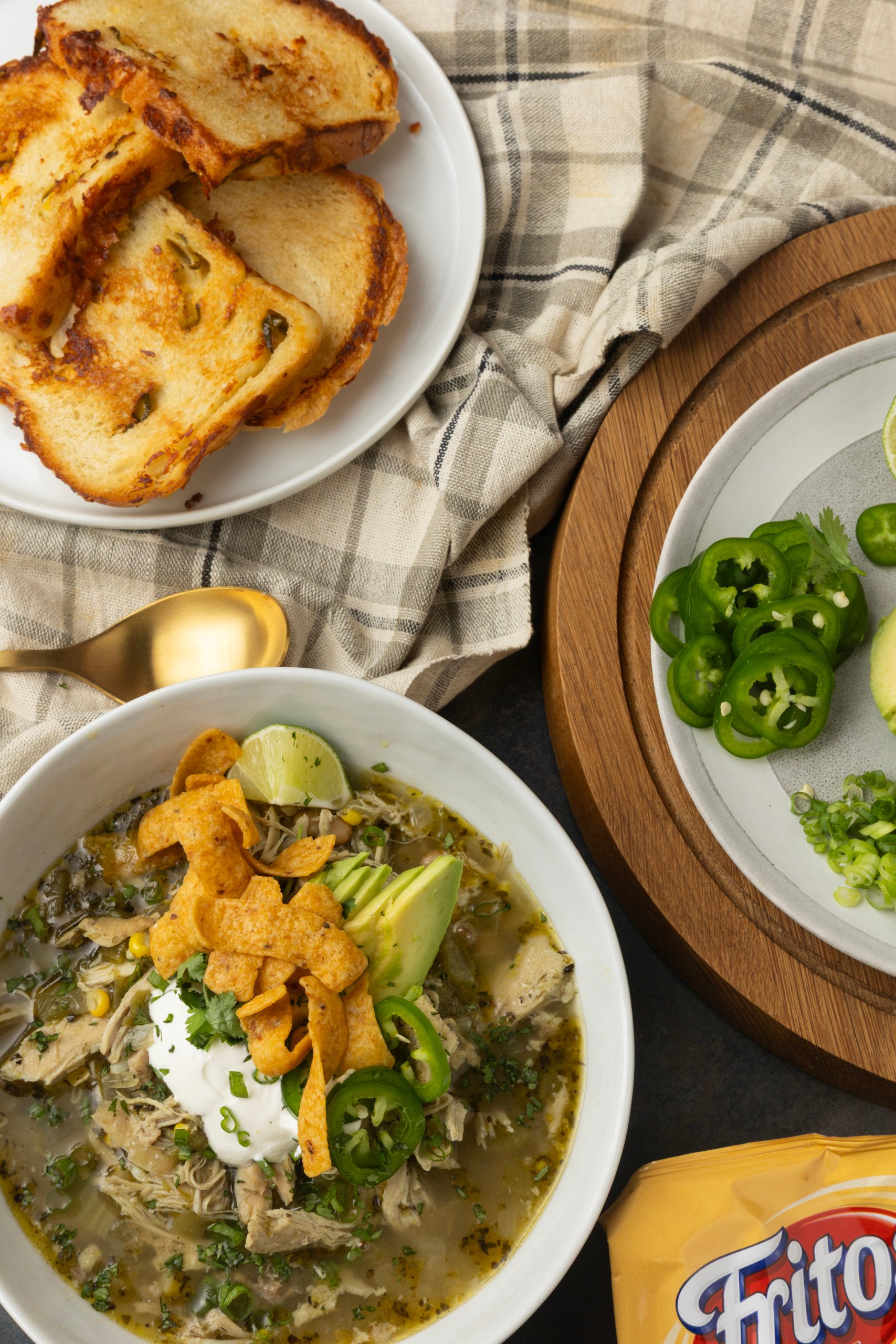 white bean chicken chili in a bowl with avocados, jalapenos, sour cream, cilantro, fritos, and lime wedges