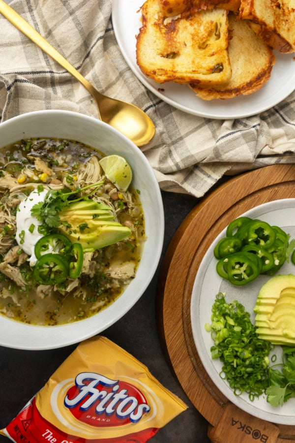 white bean chicken chili in a bowl with avocados, jalapenos, sour cream, cilantro, fritos, and lime wedges