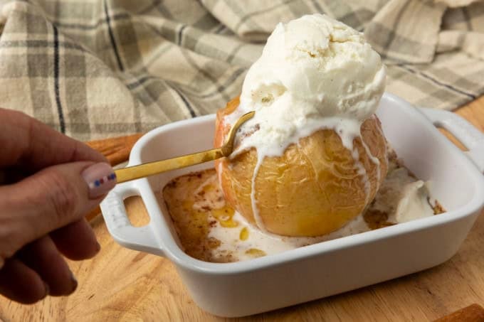old fashioned baked apple with vanilla ice cream and a hand holding a spoon