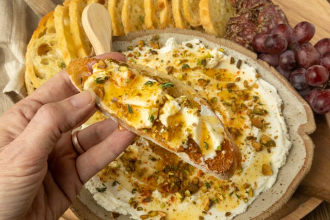whipped goat cheese appetizer in a pottery bowl with crostini, salami, and grapes