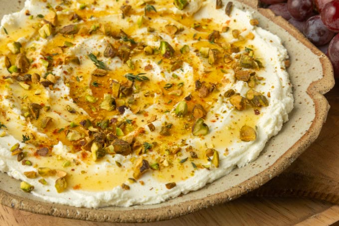 whipped goat cheese appetizer in a pottery bowl with crostini, salami, and grapes
