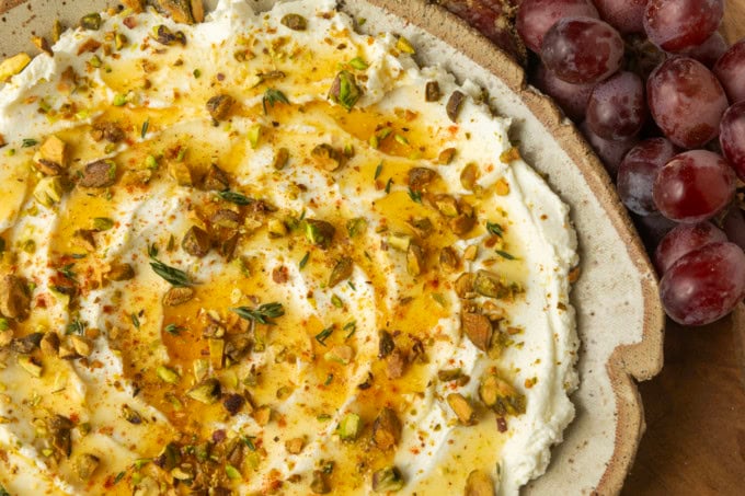 whipped goat cheese appetizer in a pottery bowl with crostini, salami, and grapes