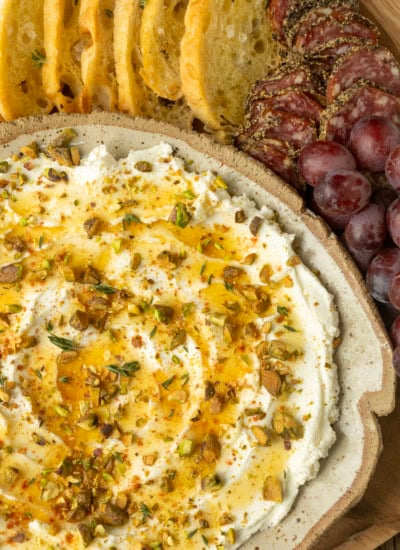 whipped goat cheese appetizer in a pottery bowl with crostini, salami, and grapes